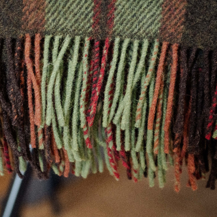 Close up of a plaid wool blanket with fringes in green, brown, orange and red colours.