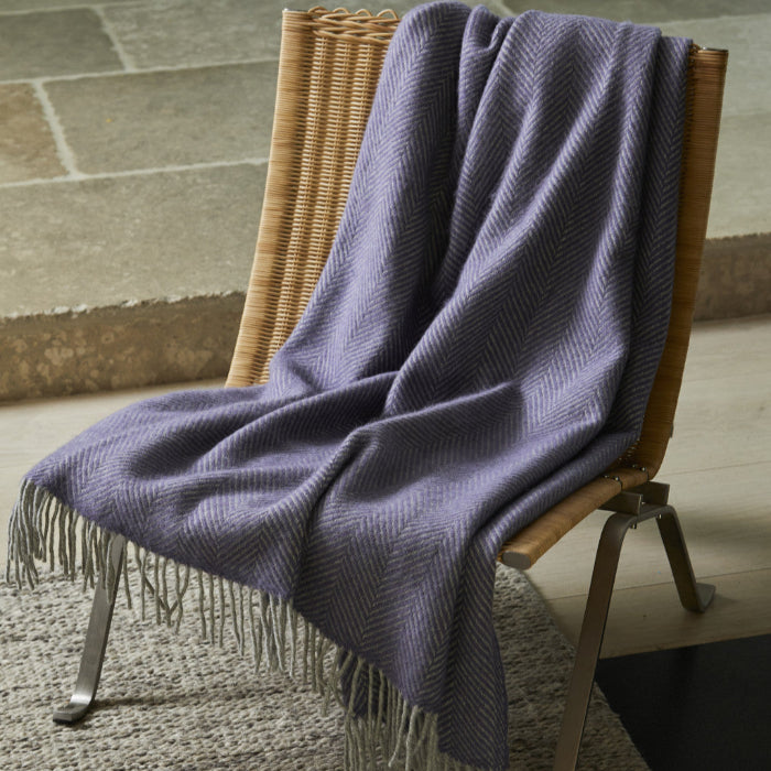 Lilac and silver herringbone style wool blanket with fringe, draped over a wooden chair with silver legs.  