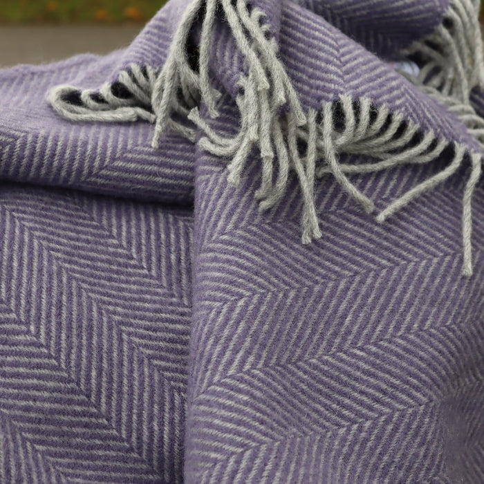 Lilac and silver herringbone wool blanket with silver fringe on a stone surface