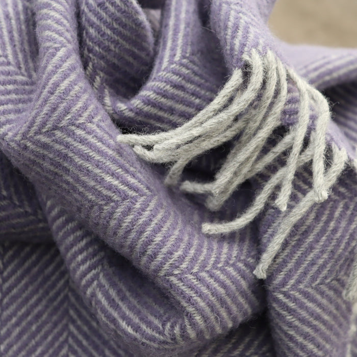 Close up of a lilac and silver herringbone wool blanket with fringe.