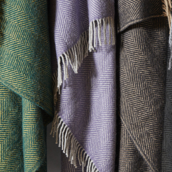 Close up of three different coloured herringbone wool blankets hanging - green, lilac and charcoal.