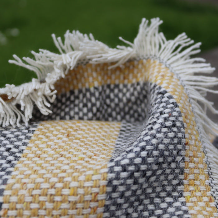 Close up of a lemon and charcoal recycled blanket with fringes on a blurred outdoor background