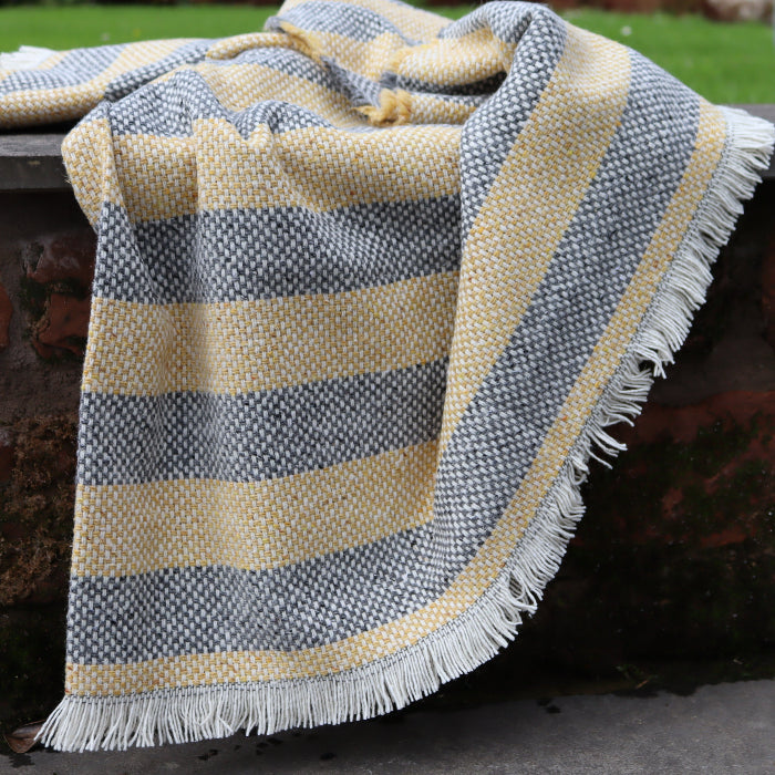 Detailed image of a recycled lemon and charcoal blanket with fringe draped over a concrete and brick wall outdoors