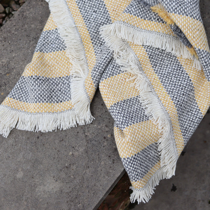 Close up of a lemon and charcoal recycled blanket with frayed fringe placed over a concrete wall