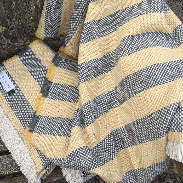 Opened out lemon and charcoal striped recycled blanket on a wooden bench outdoors