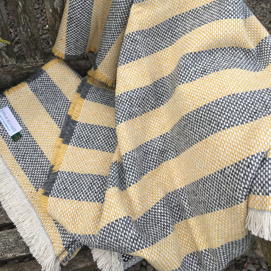 Opened out lemon and charcoal striped recycled blanket on a wooden bench outdoors