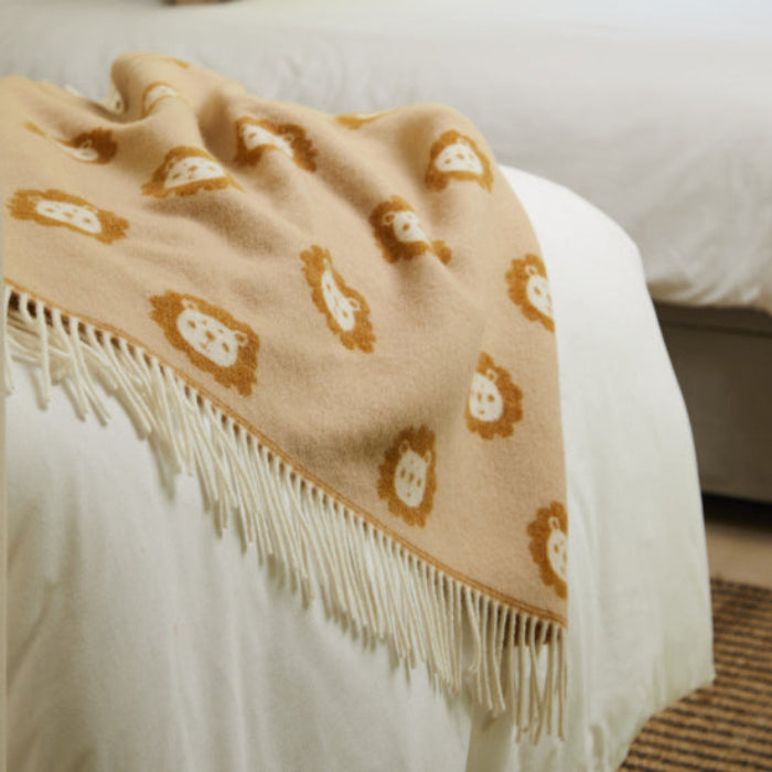 Lion Caramel Merino Wool Baby Blanket a Beige unisex baby blanket with cute lion patterns draped over a bed in a bedroom setting.