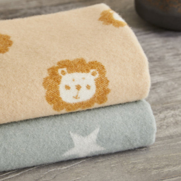 Two folded merino baby blankets, one beige with a lion design - Lion Caramel Merino Wool Baby Blanket - and one green, on a wooden surface.