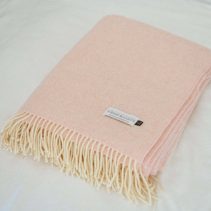 Folded pink cashmere throw with fringes on a white surface