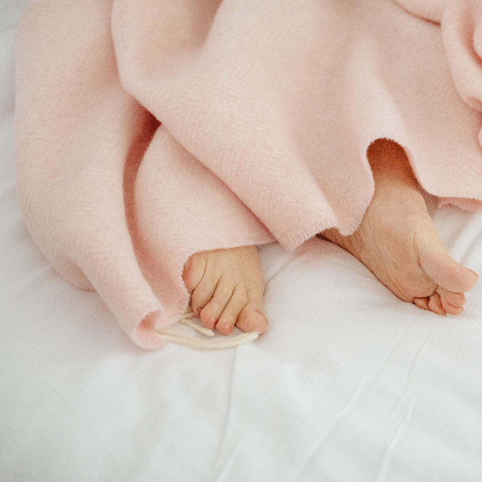Person lying on a white bed wrapped up in a pink cashmere throw with feet peeking out from underneath
