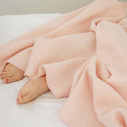 Person wrapped in a pink cashmere throw on a white bed