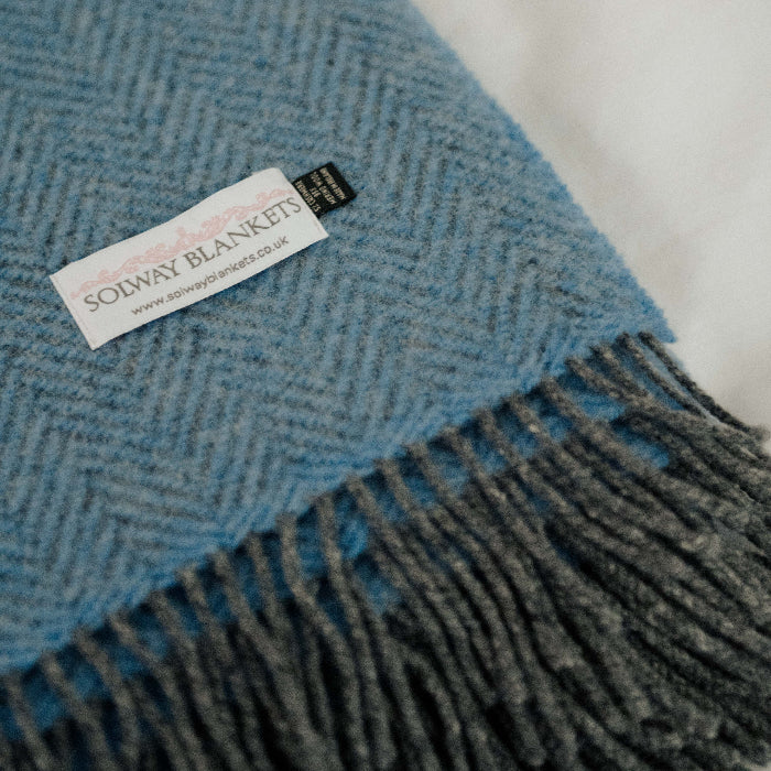 Close up blue and gray herringbone patterned cashmere throw with fringe and a Solway Blankets label on a white background