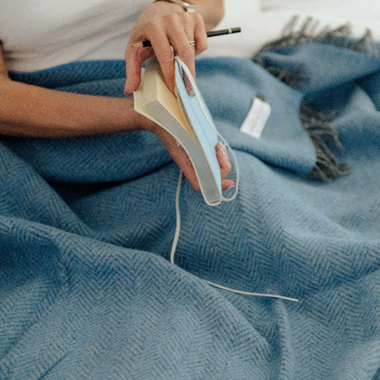 Person holding a notebook on a blue cashmere throw with a white background