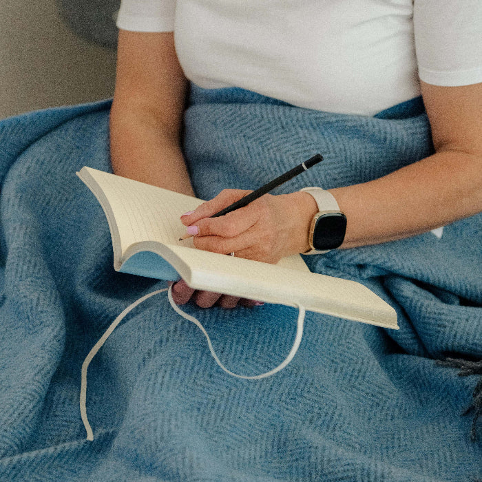 Person sitting with a blue cashmere throw holding a notebook and pencil