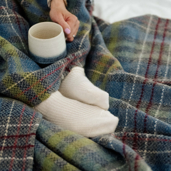 Person wrapped in a plaid throw holding a ceramic mug