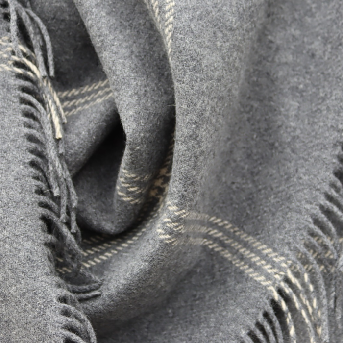 Close-up of a luxury grey cashmere blanket with cream plaid lines and fringed edges, draped to show texture and pattern.
