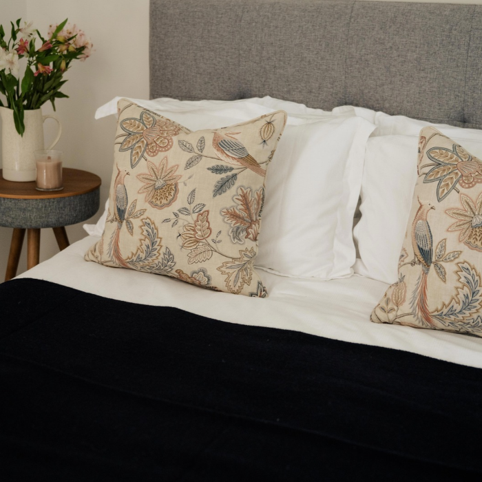 Moffat Midnight pure cashmere throw in deep navy blue with fine weave and fringed edge, styled on a bed with patterned cushions, next to a side table with flowers.