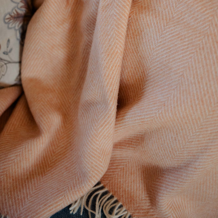 Close-up of a textured peach coloured throw. The Mango Sorbet Shetland Wool Herringbone Blanket draped on a sofa. 
