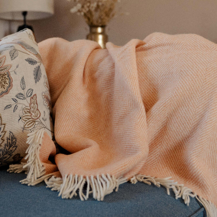 Mango Sorbet Shetland Wool Herringbone Blanket throw blanket on a blue sofa with printed cushion 