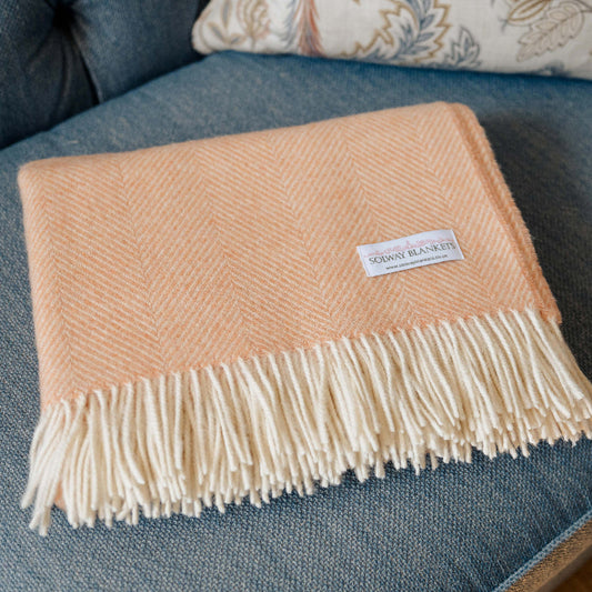 Mango Sorbet Shetland Wool Herringbone Throw Blanket with fringe on a blue couch
