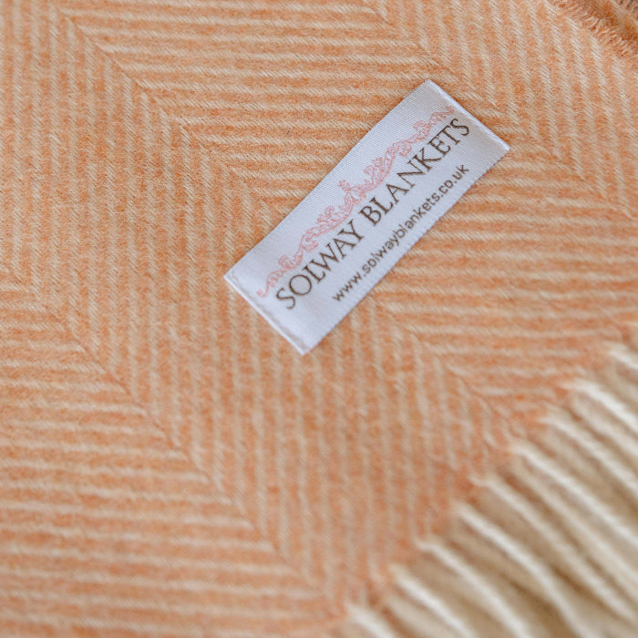 Close up of a Solway Blankets label on a mango coloured herringbone pattern wool blanket with fringe