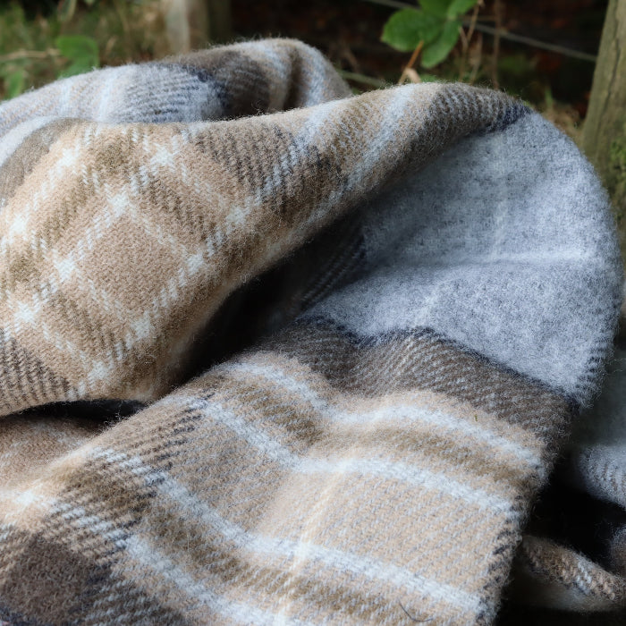 Neutral grey and light brown Mckellar Tartan woollen knee blanket draped over a log with a natural outdoor background