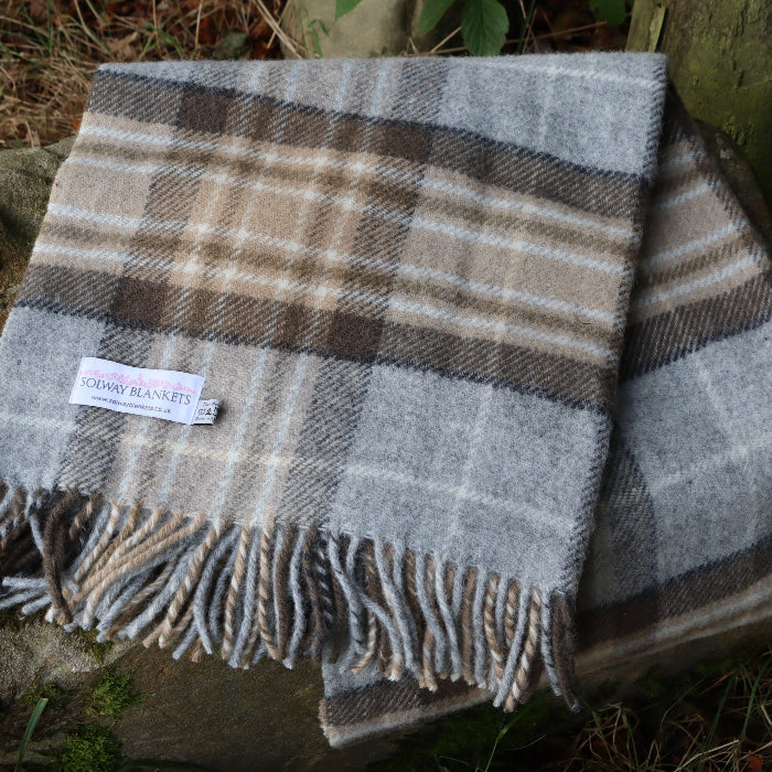 Neutral coloured McKellar tartan woolen blanket with fringes on a stone surface, outdoors, featuring a Solway Blankets label