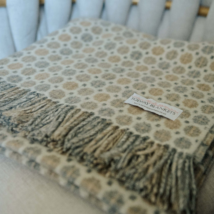 Neutral patterned throw blanket with fringe folded neatly on a chair, featuring a Solway Blankets label.