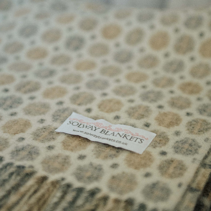 Close up of a natural patterned throw with a visible Solway Blankets label on a neutral background