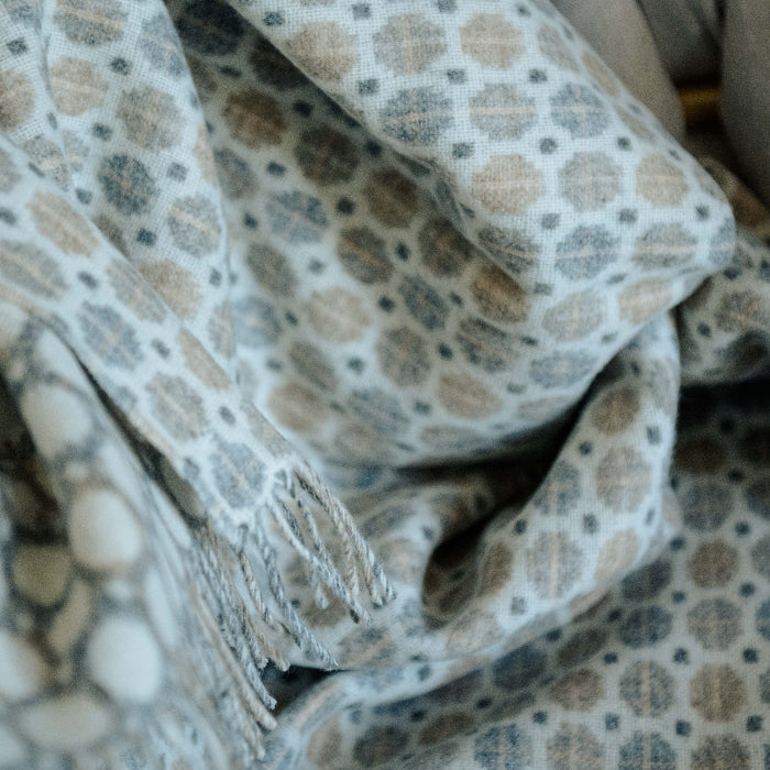 Close up of a patterned fabric throw with beige and brown colors and a fringe. 