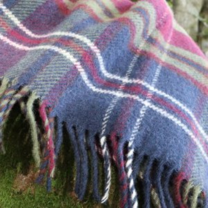 Close up of a morello cherry tartan plaid wool blanket with a fringe on a grassy background