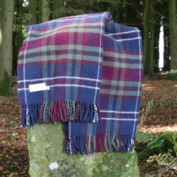 Morello Cherry Plaid pure wool blanket draped over a stone with a forest background
