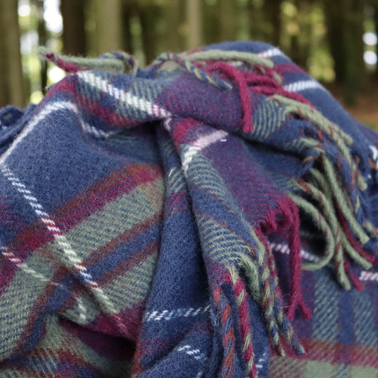 Morello Cherry wool small blanket featuring colours of cherry, blue and green with fringes in a forest setting