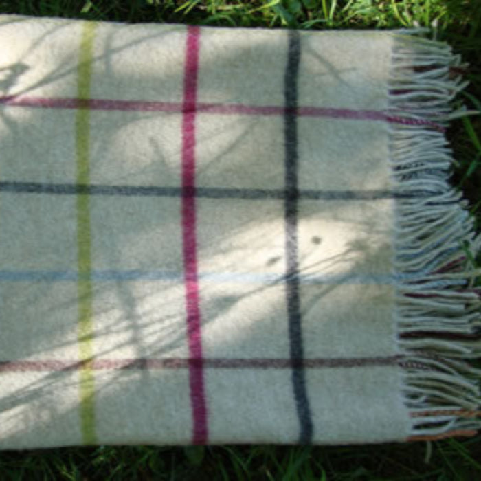 Multicoloured check merino lambs-wool blanket with fringe, folded on top of grass