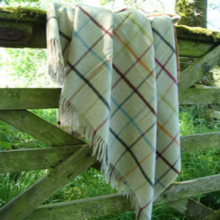 Multicoloured plaid merino blanket draped over a wooden gate with greenery in the background