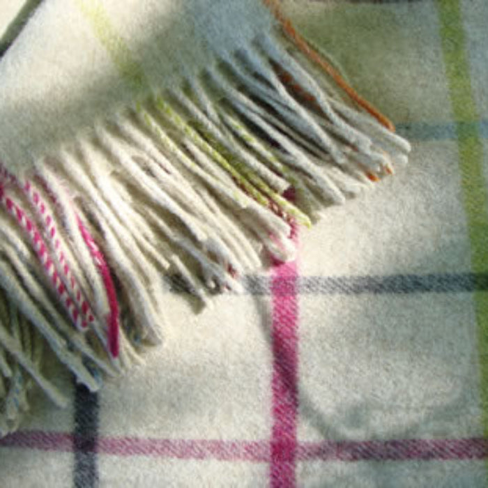 Multicoloured merino lambs-wool blanket with fringe, featuring colours of crimson, charcoal, burnt umber, lime green, blue and orange against a beige background. 