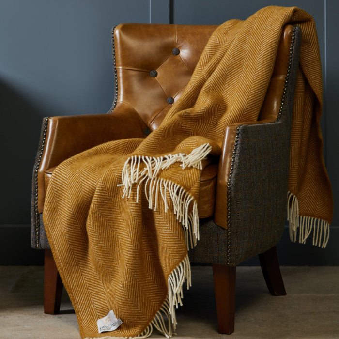 Brown leather and grey fabric armchair, with a mustard yellow fishbone wool blanket draped over it against a dark blue wall.