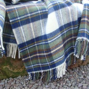 Muted Blue Stewart Tartan Plaid natural wool traditional blanket with fringe on a stone surface