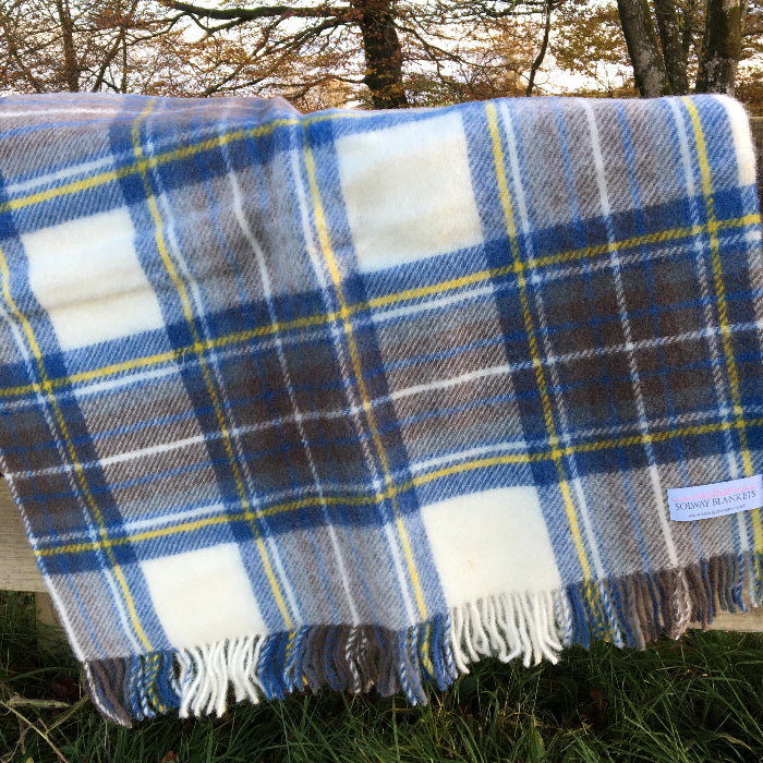 Blue and green tartan pure wool lap blanket for armchair, with fringe and a Solway Blankets label, folded out over a wooden fence outdoors
