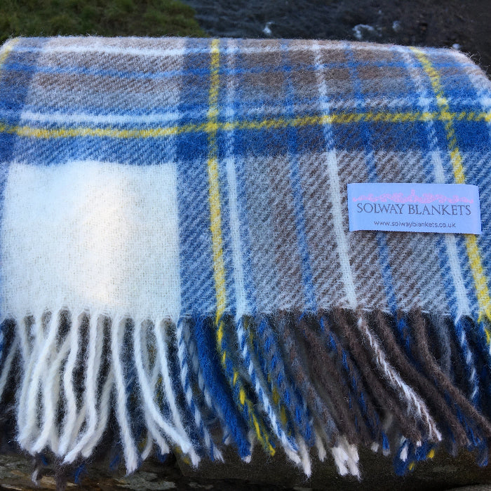 Close up of a folded muted blue tartan woolen knee rug, featuring a Solway Blanket label