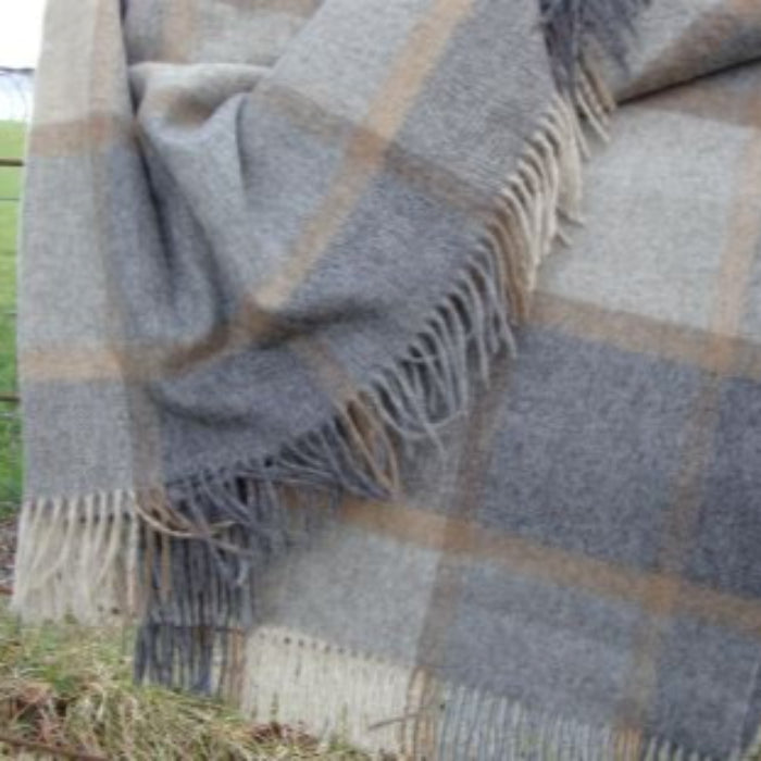 Natural plaid blanket with fringes draped over a fence on a grassy background
