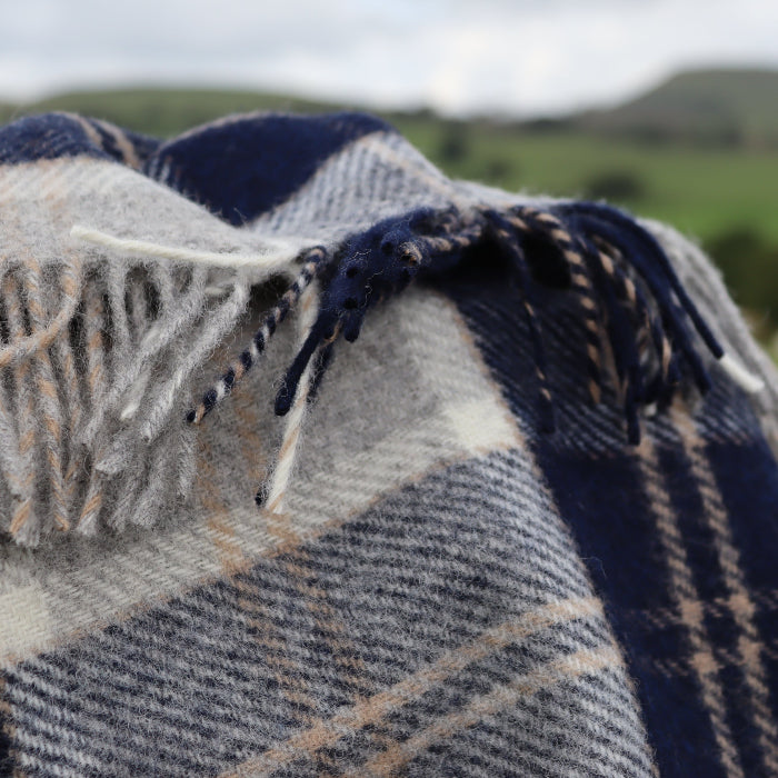Plaid blanket with fringe draped over a surface with a blurred natural landscape in the background