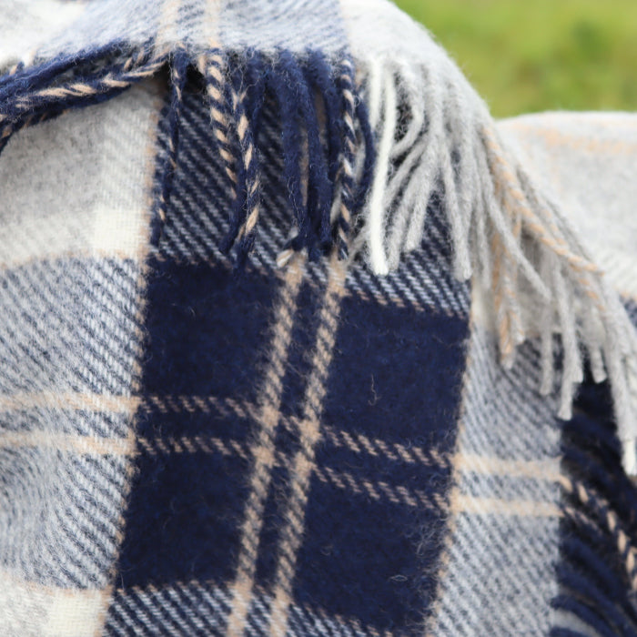 Close-up of a navy and white plaid blanket with fringes on a blurred natural background