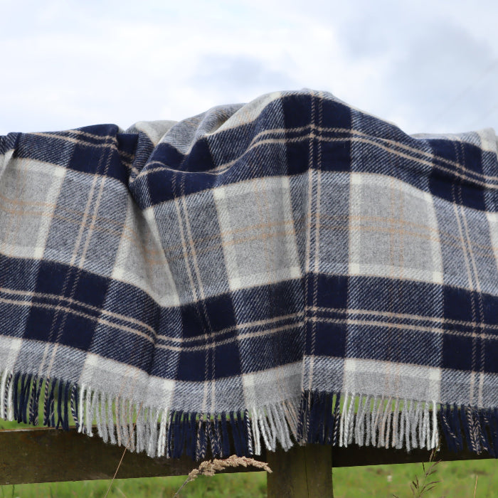 Navy, white and beige wool plaid blanket with fringes draped over a wooden fence in a rural setting