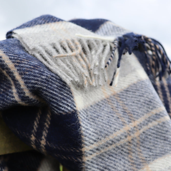 Plaid navy, white and beige blanket throw with fringe on a wooden fence outdoors
