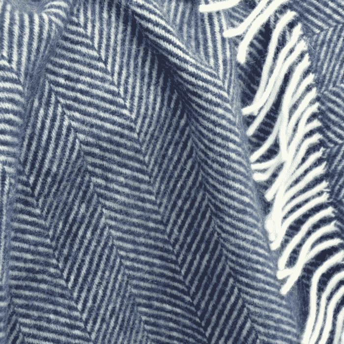 Detailed close up of a navy blue fishbone wool blanket with white fringe