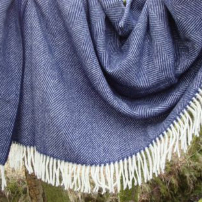 Navy blue woven herringbone blanket with white fringe draped over a natural background