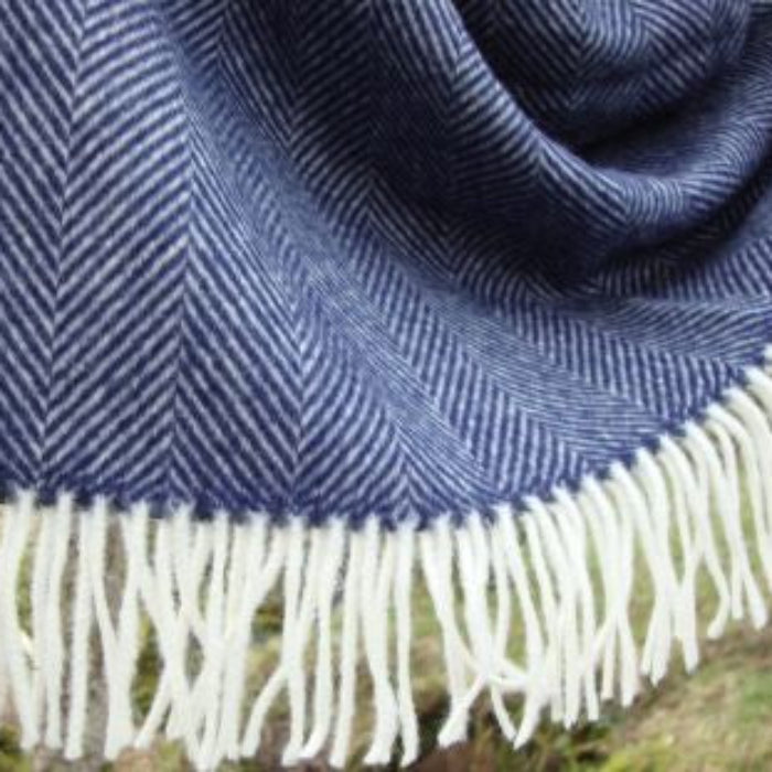 Close up of a navy blue herringbone blanket with white fringe on a grassy background