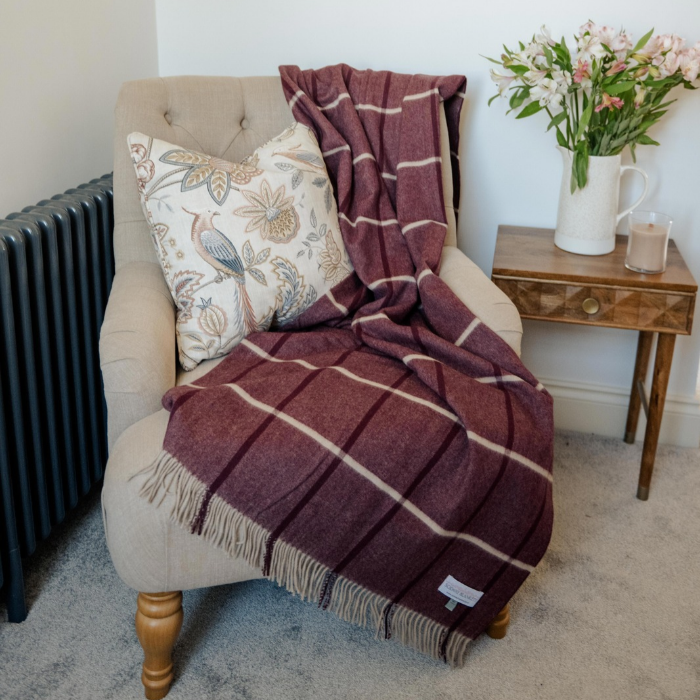 Luxury Scottish woven plum and ivory cashmere blanket folded on a cream upholstered armchair