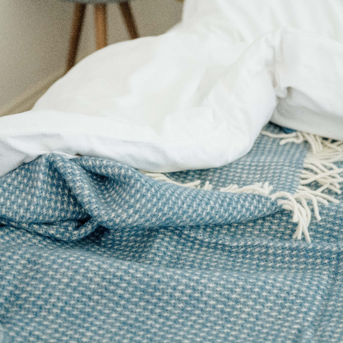 Ocean blue waffle textured wool blanket with white fringe draped over a white bed